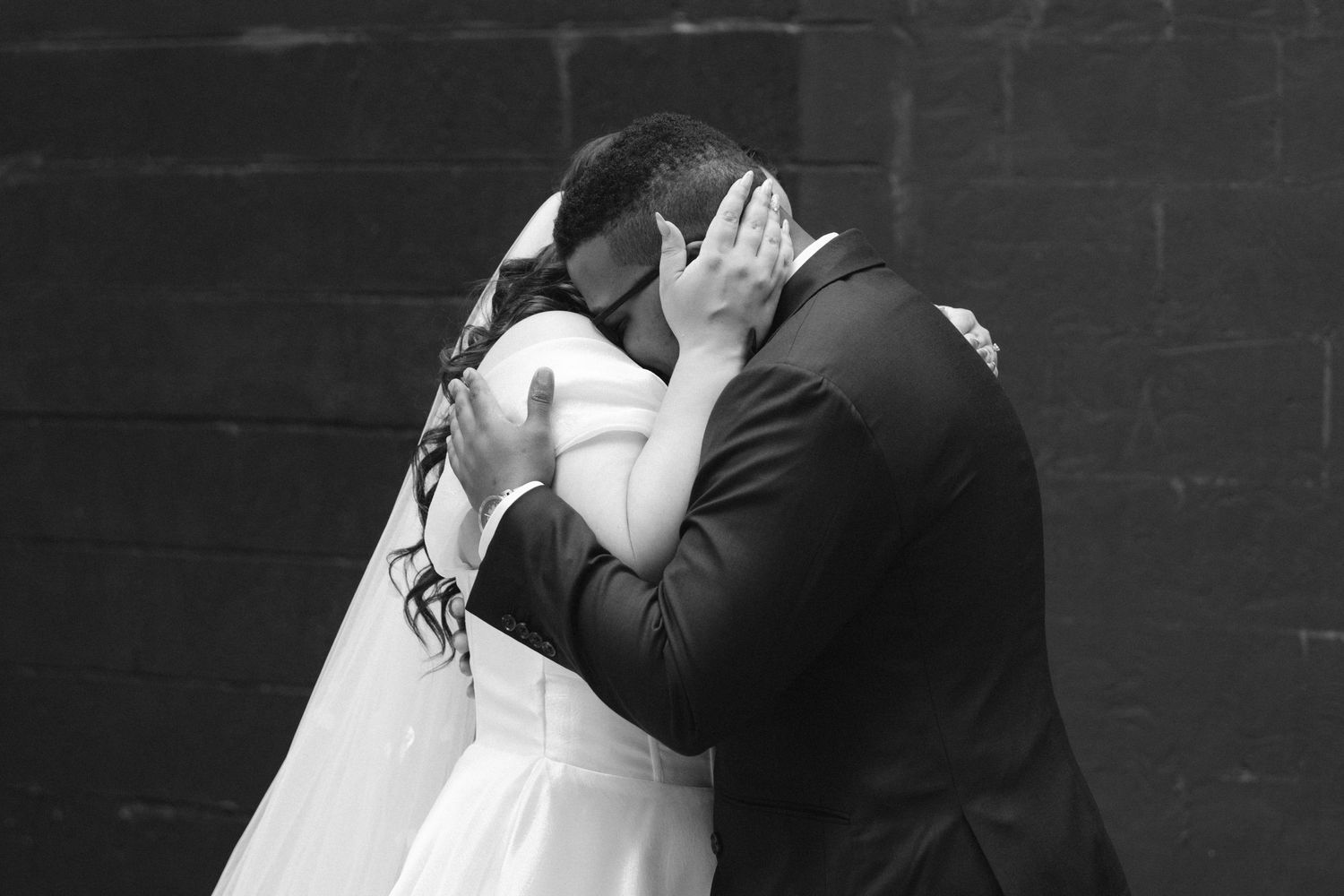 Black and white photo of a bride and groom sharing a romantic kiss on their wedding day.