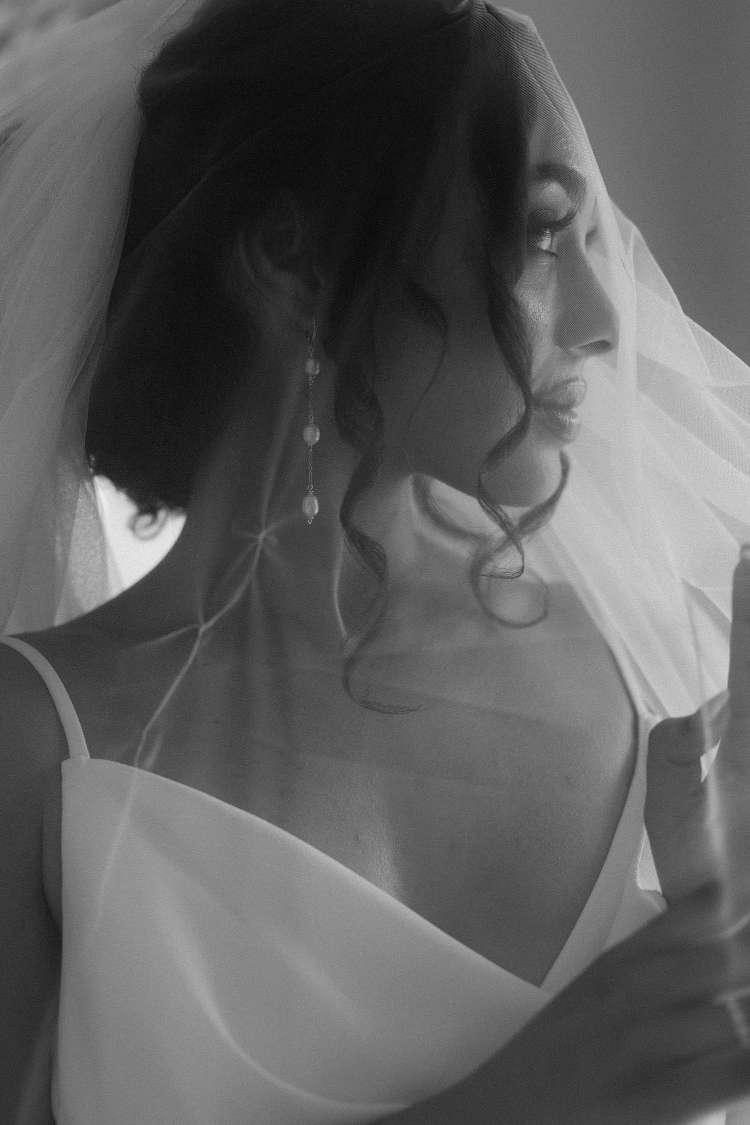 Black and white portrait of a bride in a wedding veil and gown, showcasing elegant pearl earrings and curled hair.