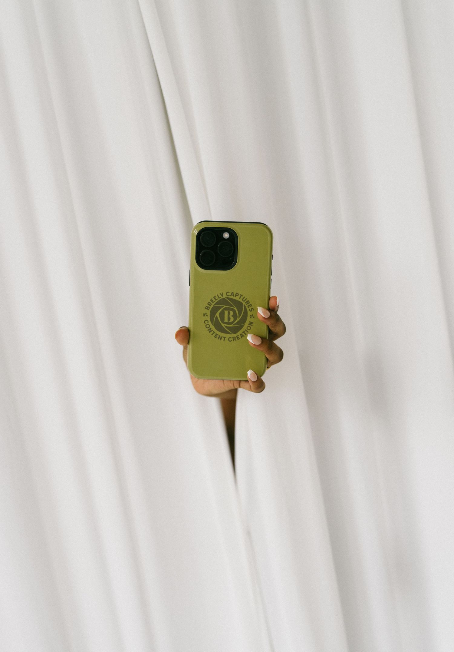 Hand emerging from white curtains holding an olive green branded smartphone case.