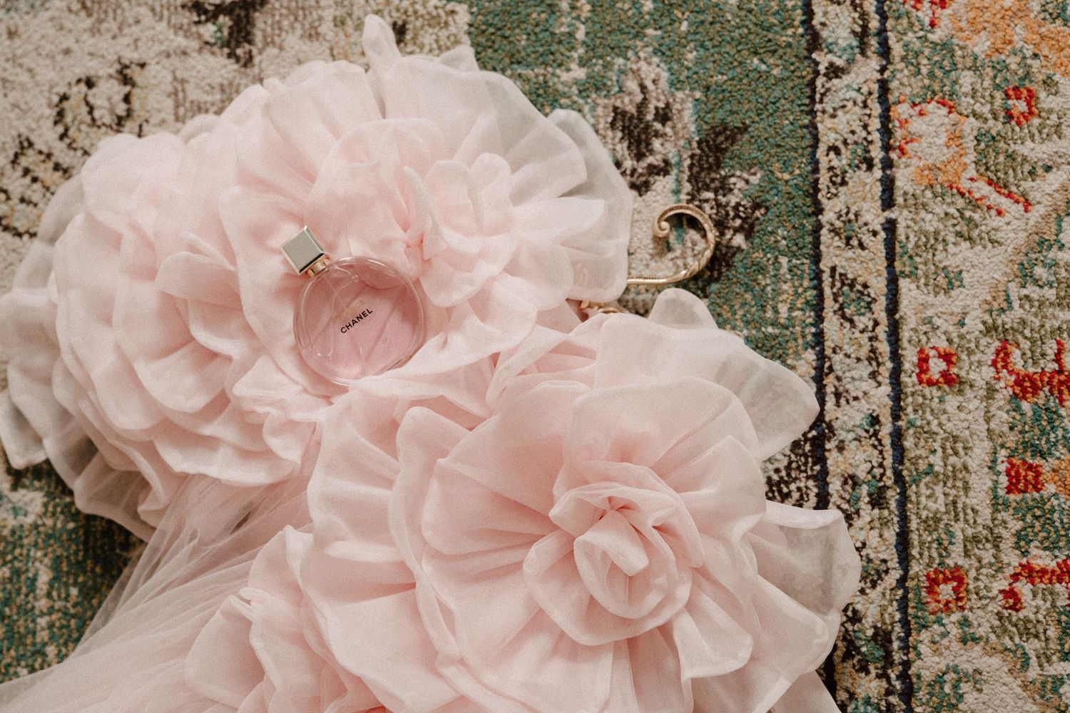 Pink chiffon flower embellishments on a floral patterned rug, featuring layered ruffled petals in soft blush tones.
