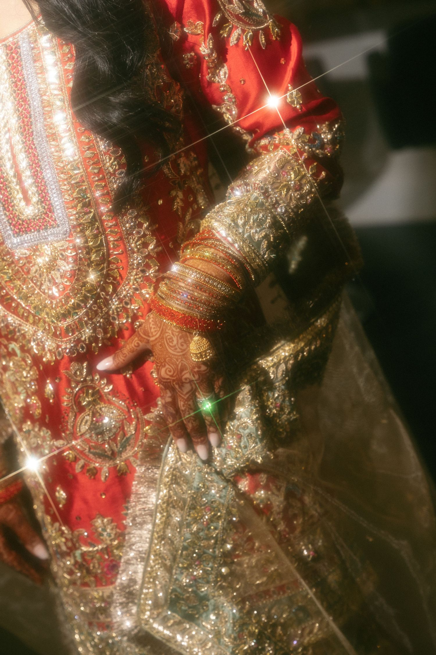 Close-up of a bride in ornate red and gold Indian bridal attire with intricate mehndi, bangles, and embroidered dupatta.