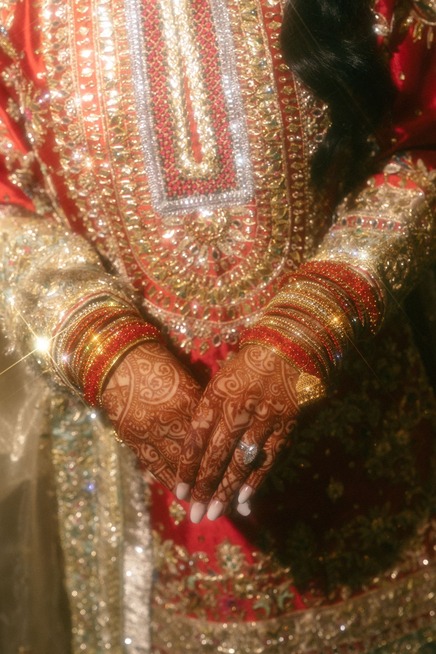 Indian bride's hands adorned with intricate mehndi henna designs and colorful bangles, wearing ornate embroidered bridal attire.