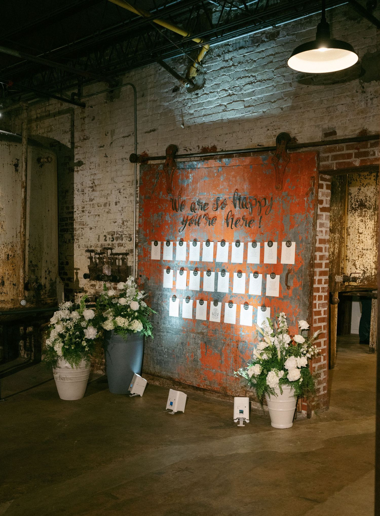 Rustic industrial wedding seating chart displayed on a vintage sliding barn door with white floral arrangements.
