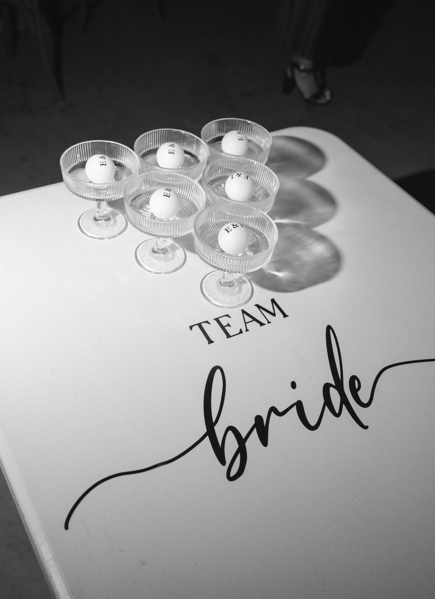 Black and white photo of coupe glasses with candles on a Team Bride sign at a bachelorette party.