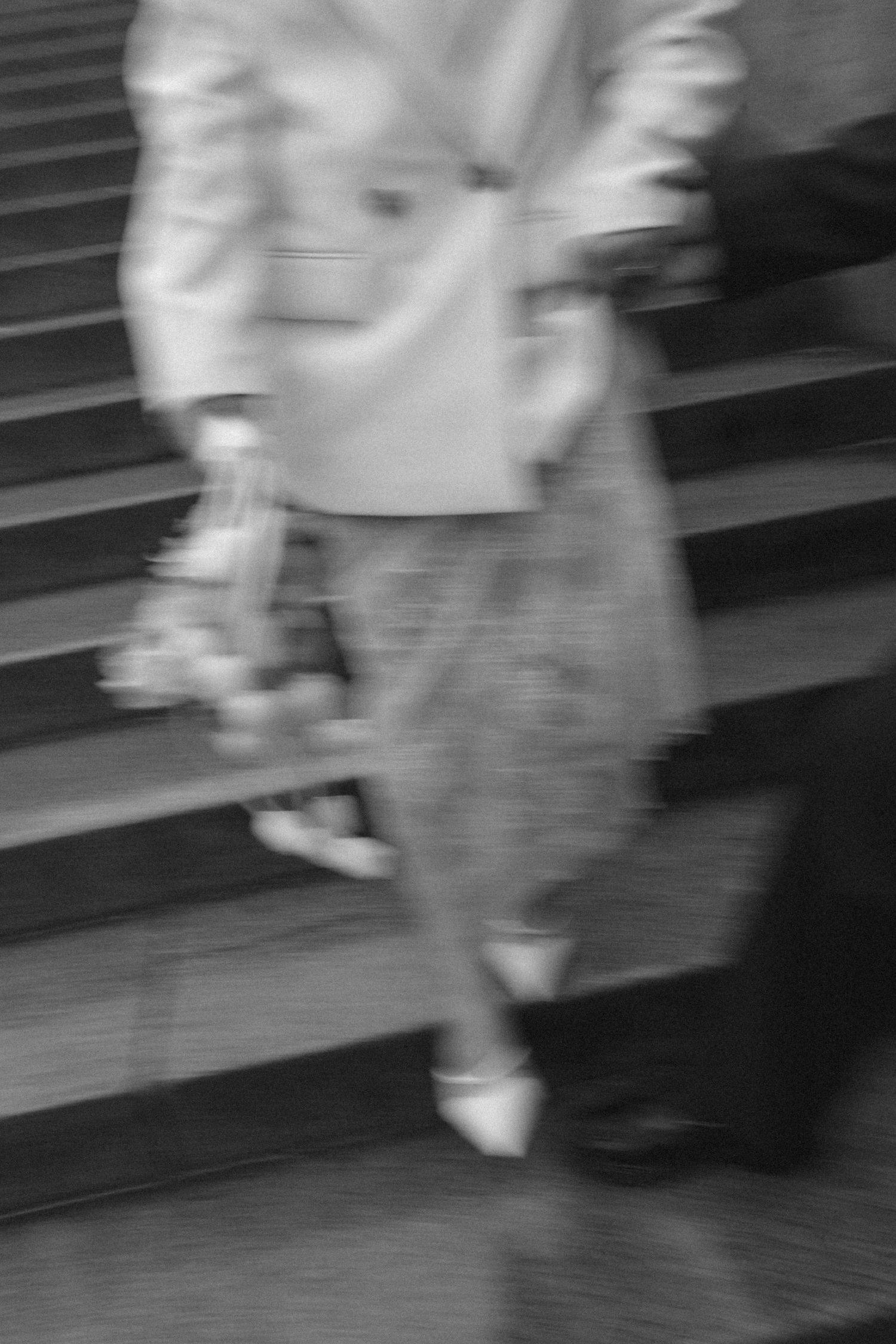 Blurry black and white photo of a woman in a blazer and skirt holding flowers while descending stone steps.