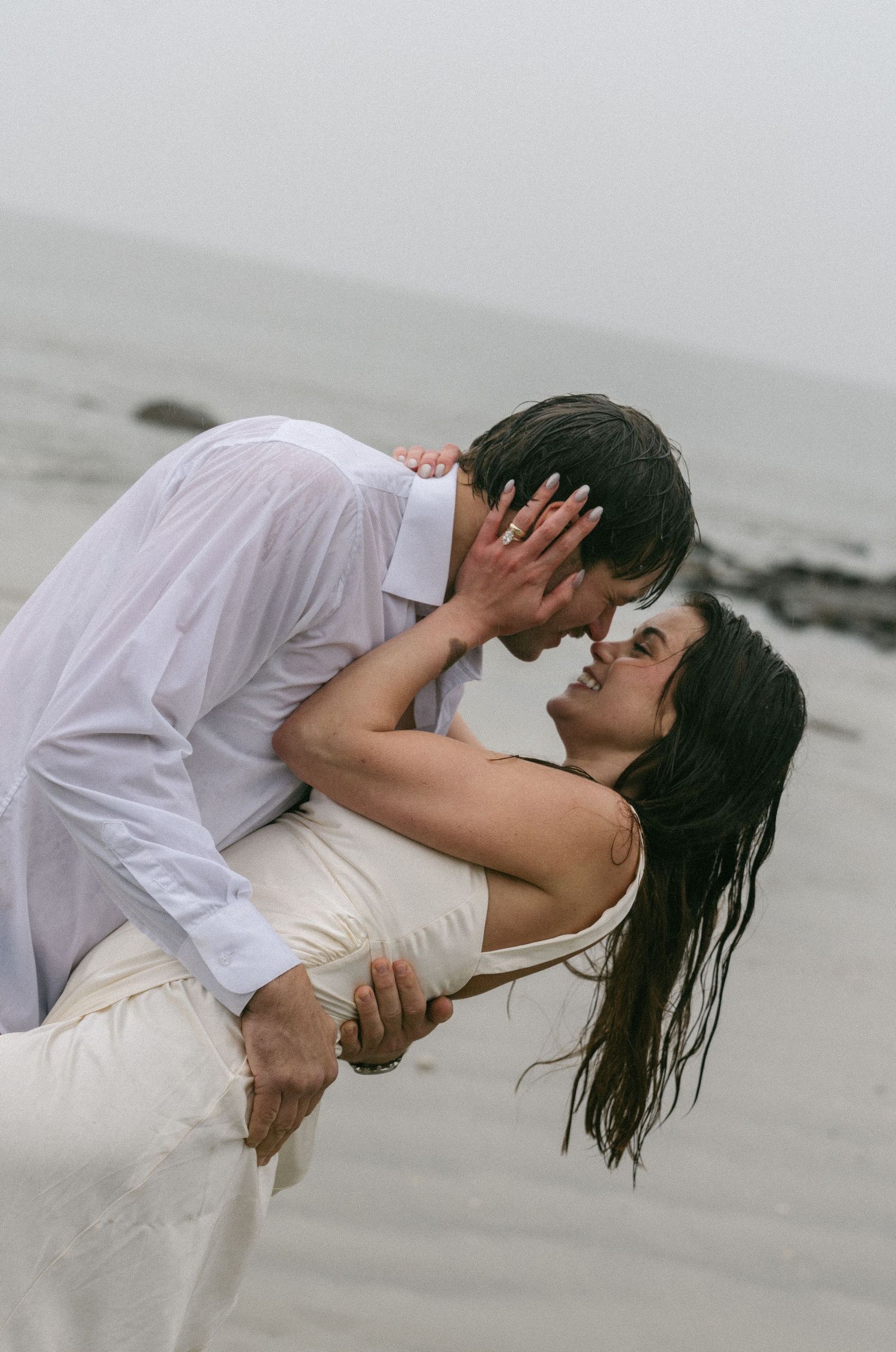 Jekyll Isalnd Engagement Shoot Couple sharing a romantic dip kiss on a misty beach, bride in white dress and groom in white shirt.