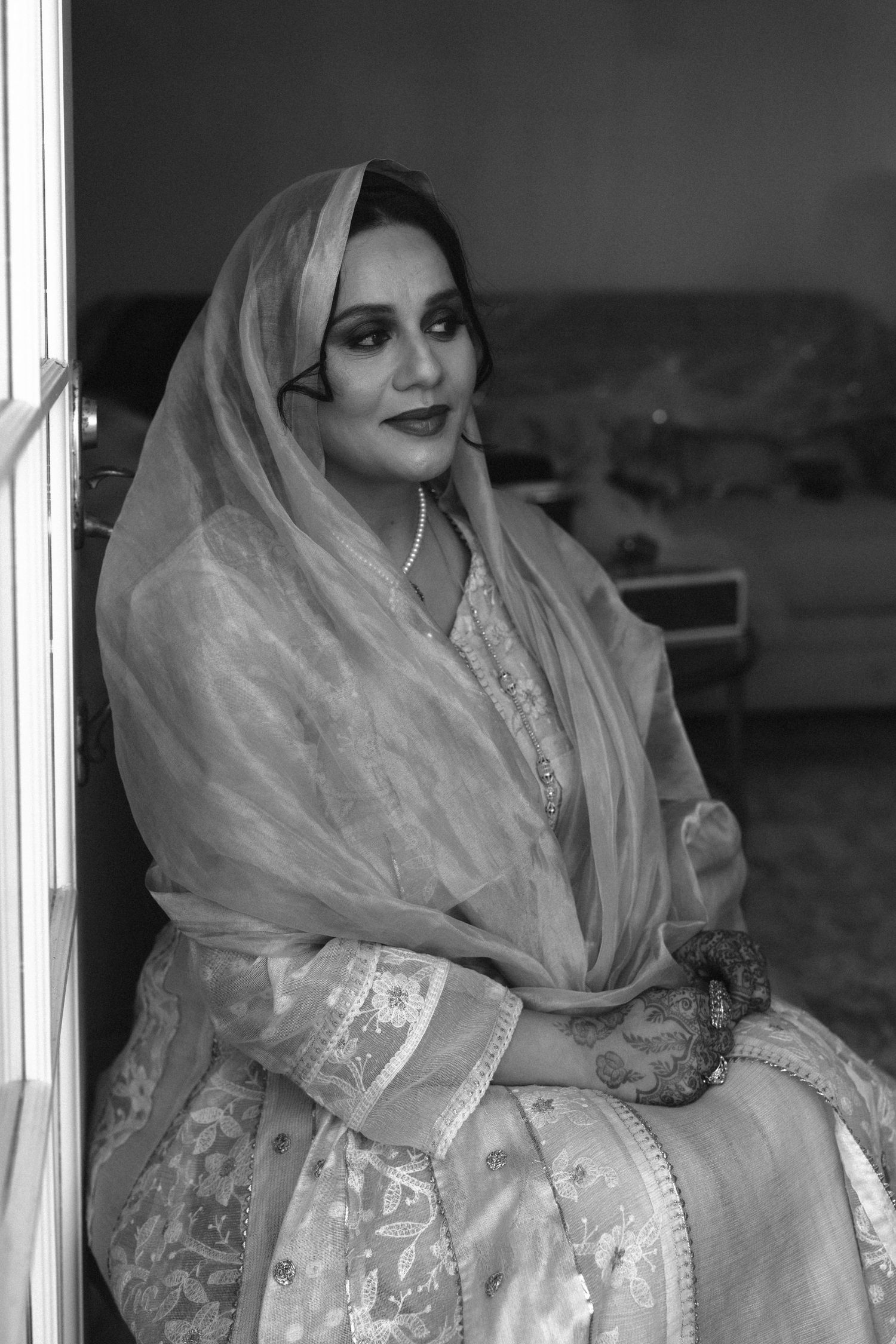 Black and white portrait of a woman in traditional South Asian attire with dupatta and mehndi, seated gracefully.