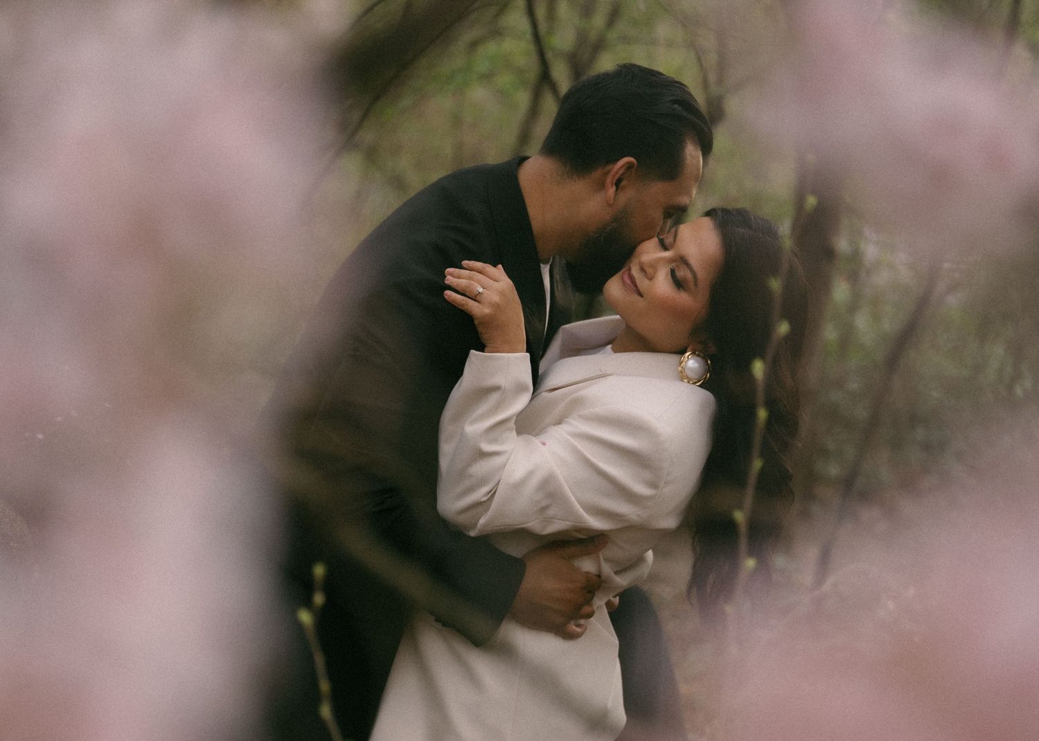 Couple sharing a romantic embrace surrounded by soft pink blossoming flowers in a dreamy outdoor spring setting. Central Park NYC