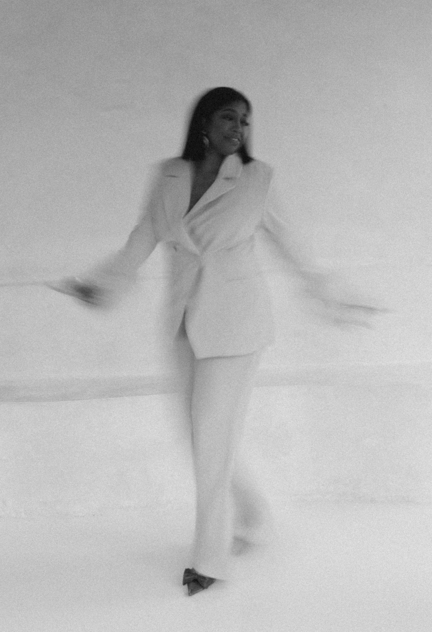 Black and white photo of a woman in a white suit dancing with motion blur against a light background.