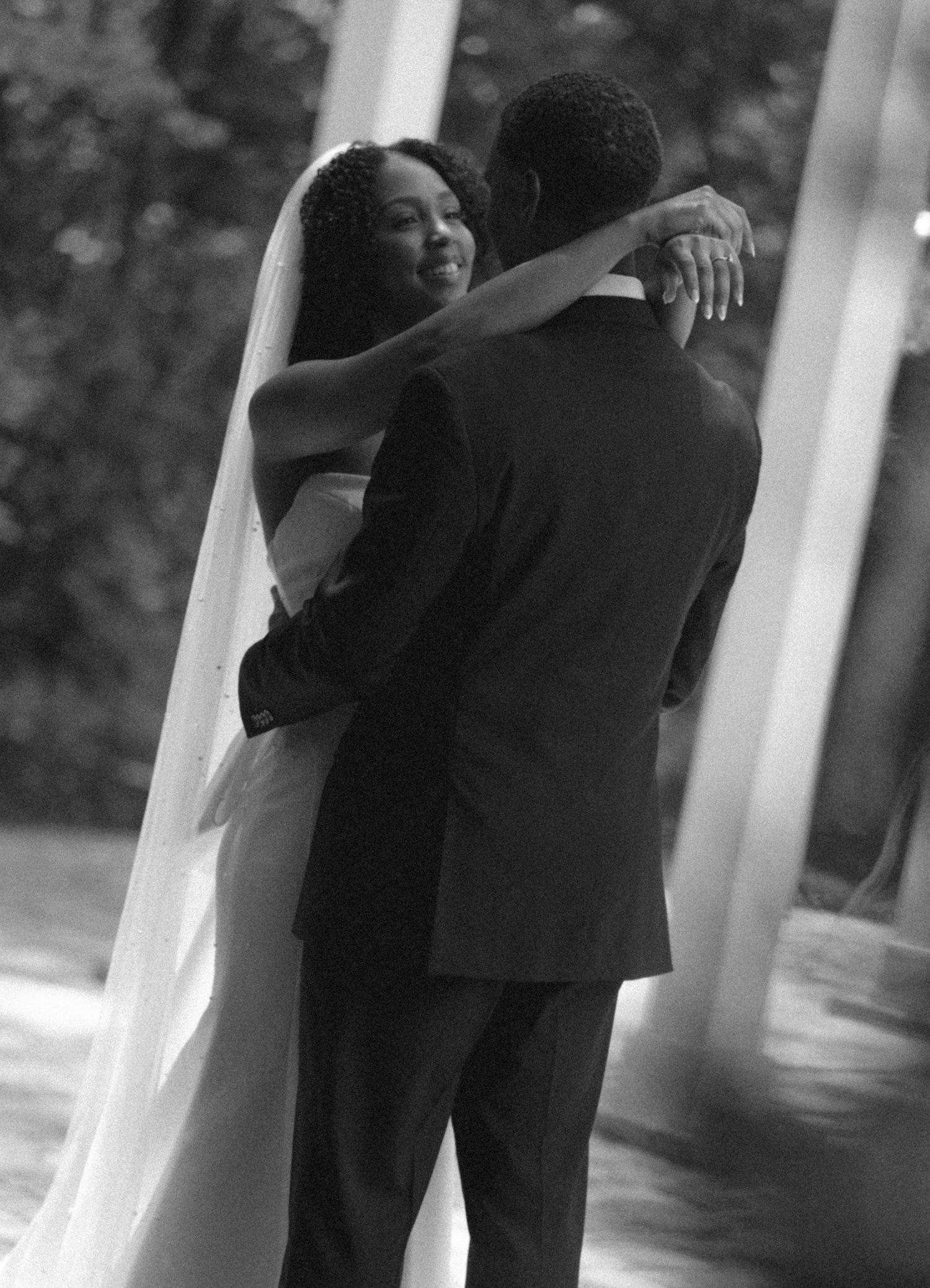 Black and white photo of bride and groom sharing first dance near elegant white columns.