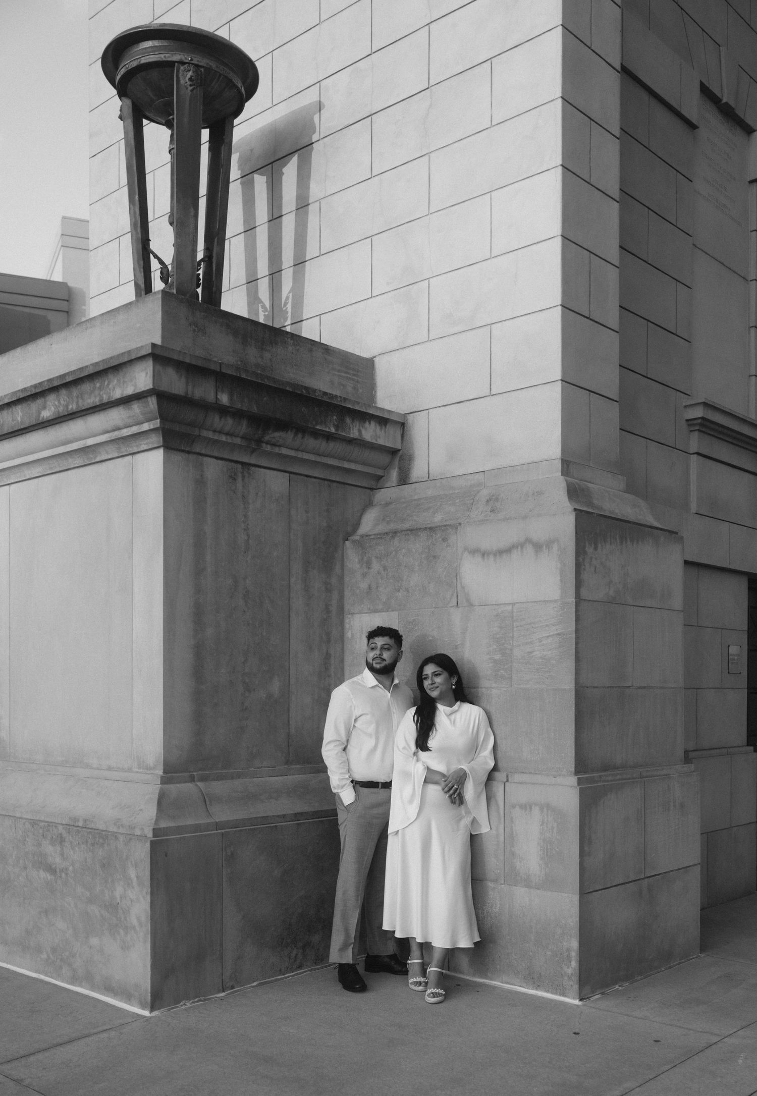 Black and white photo of a couple standing together by a stone building.