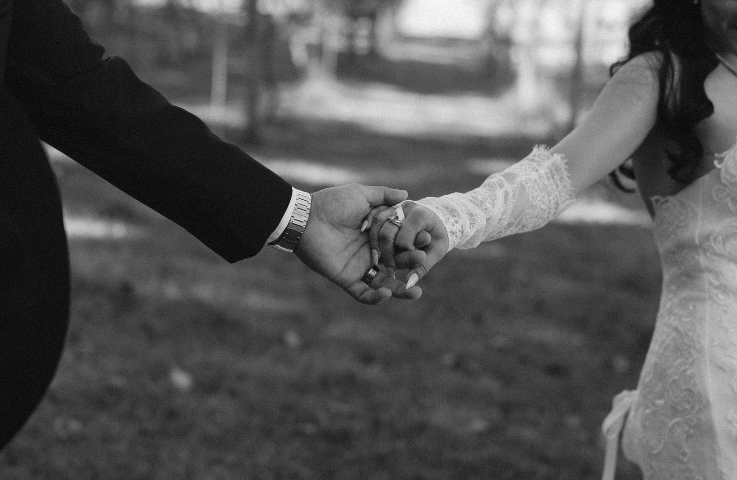 Black and white photo of a bride and groom holding hands outdoors on their wedding day.