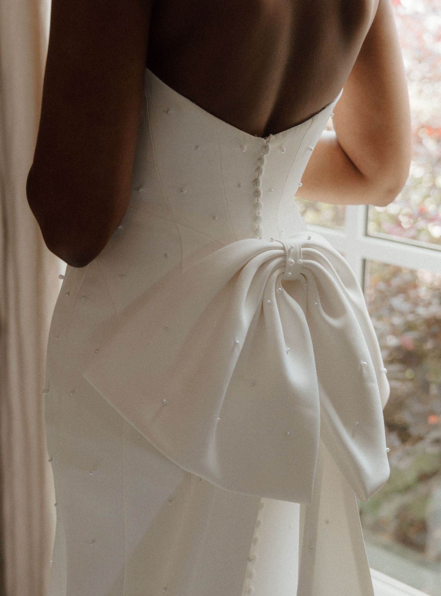 Close-up of a white wedding dress featuring pearl details, button back closure, and an elegant oversized satin bow.