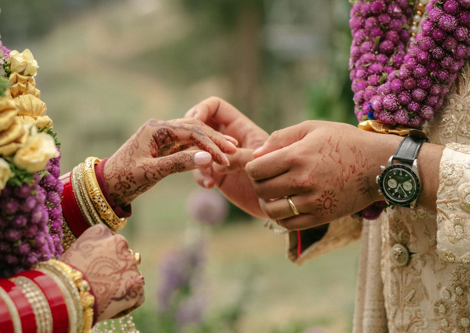 Indian bride with henna hands and bangles placing ring on groom during traditional Hindu wedding ring exchange ceremony.