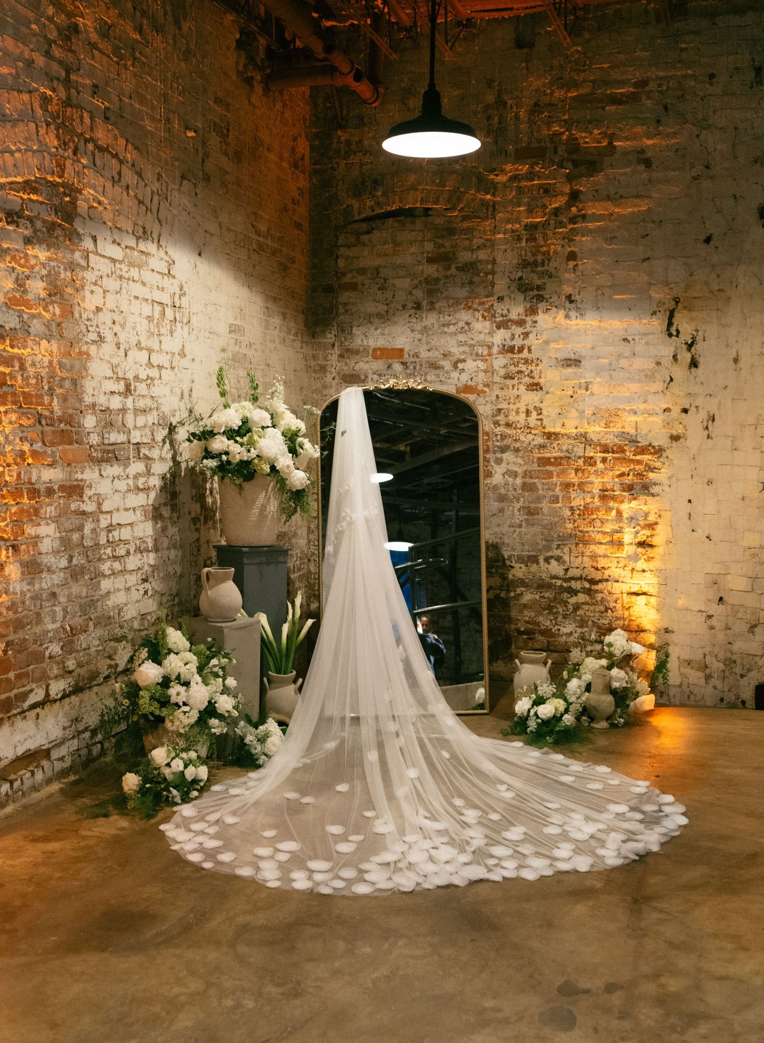 Elegant bridal veil with floral appliques displayed against rustic brick walls with white flower arrangements in a moody venue.