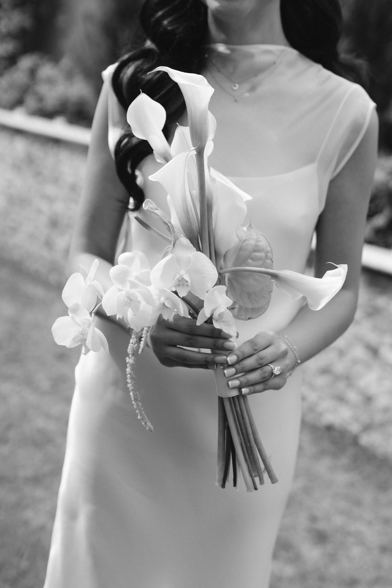 Bride in white gown holding elegant bouquet of calla lilies and orchids, black and white wedding photo.