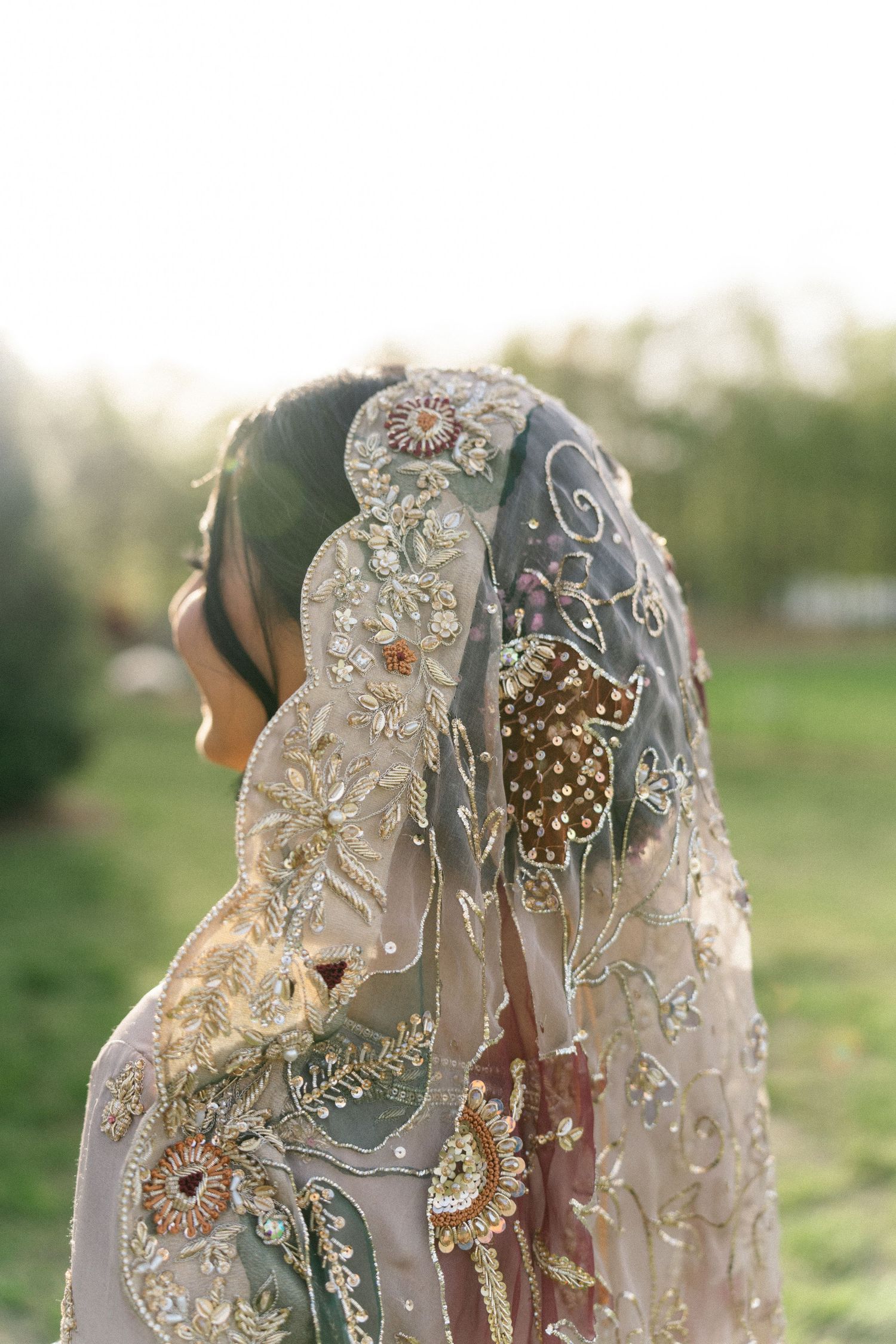 Woman wearing an ornate embroidered dupatta with floral beadwork and sequins, photographed outdoors in soft sunlight.