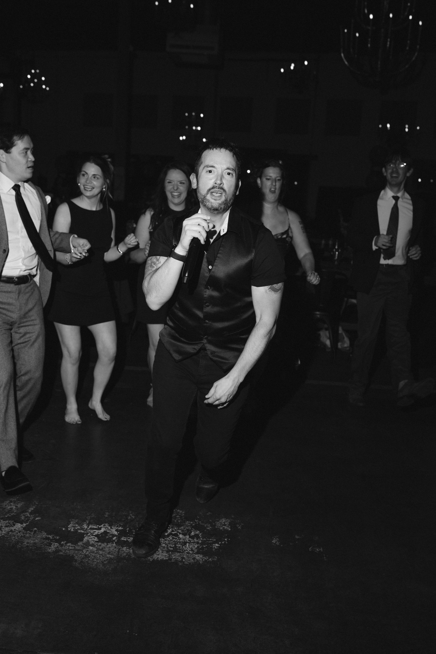 Man energetically dancing at a wedding reception while guests celebrate in the background.