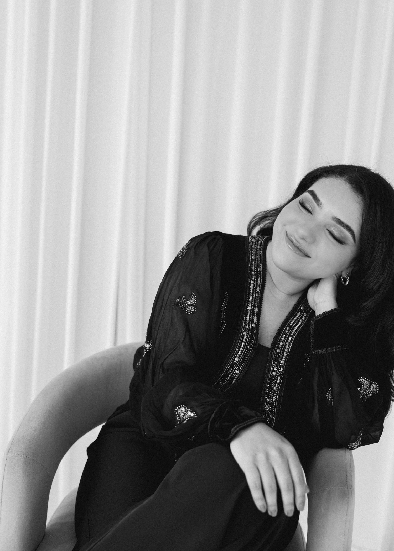 Black and white photo of a young woman in a sequined black blouse, relaxing in a chair with eyes closed.