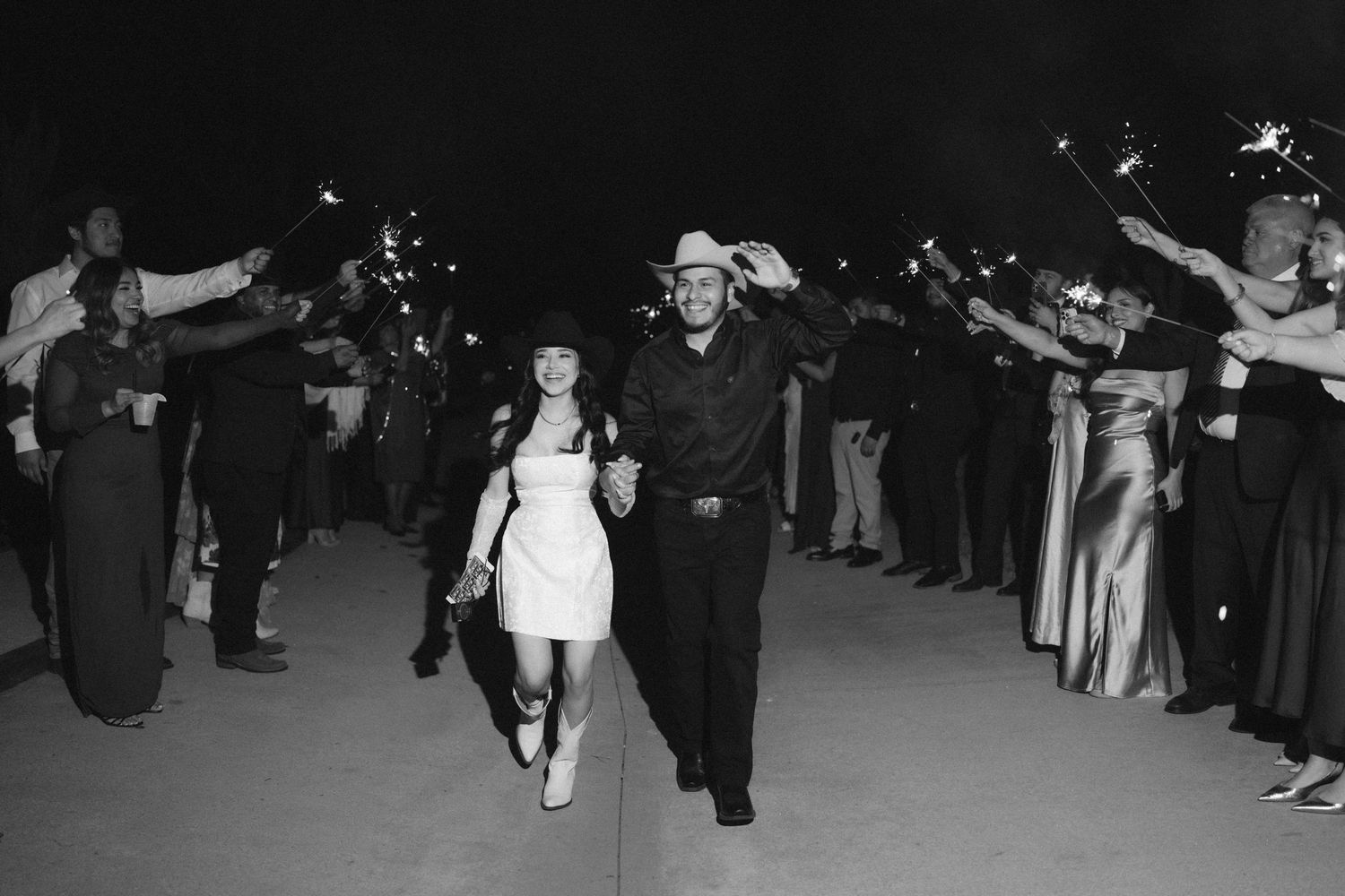 Bride and groom walk through sparkler sendoff at night wedding celebration in black and white photo.