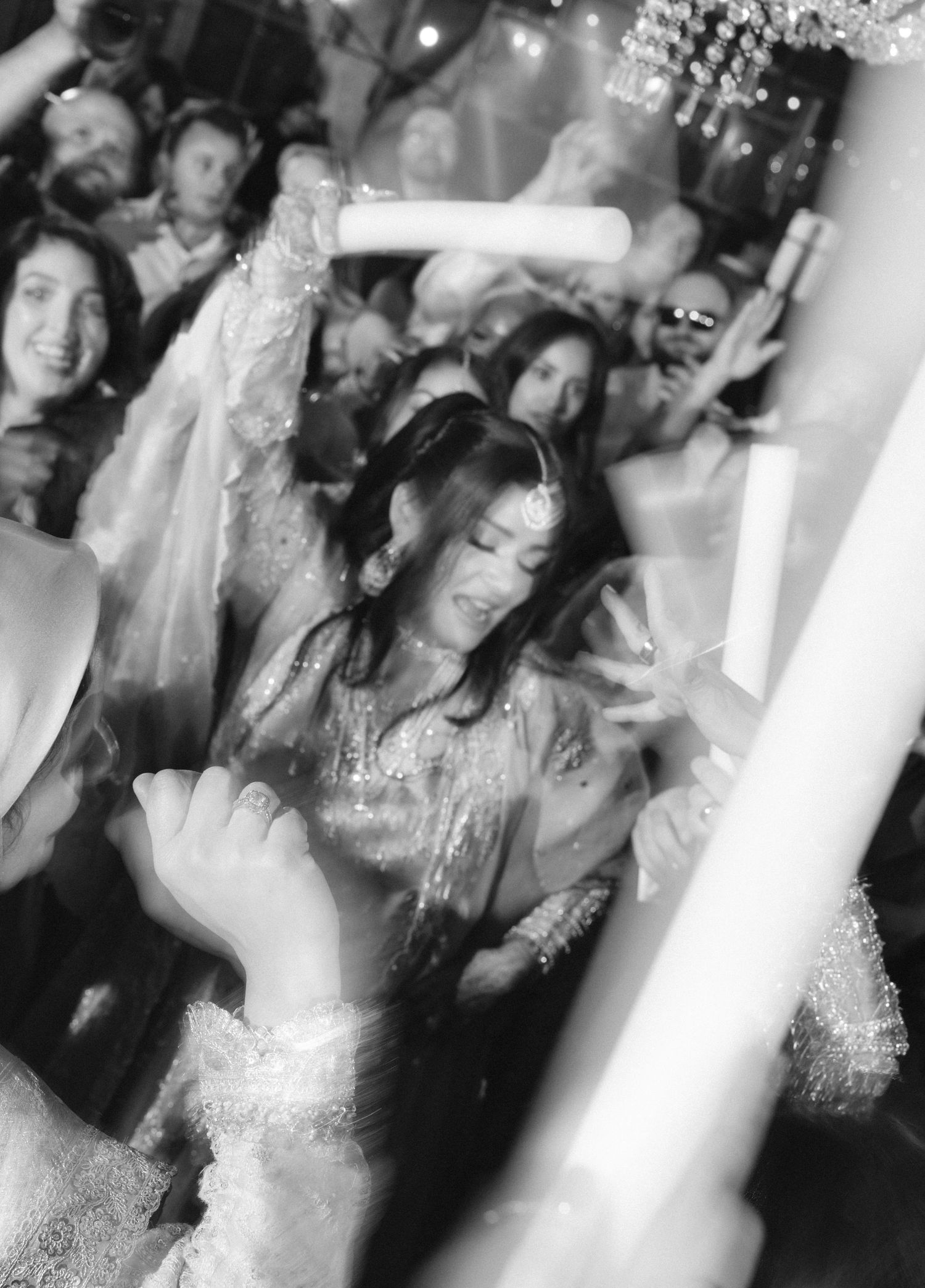 Black and white photo of a woman dancing joyfully at a festive celebration surrounded by guests.