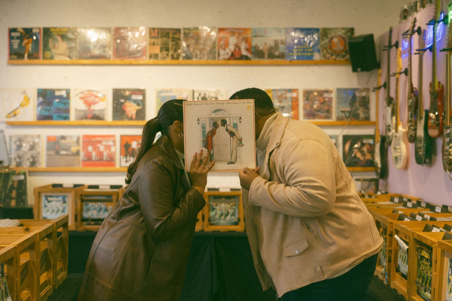 Couple browsing vinyl records together in a colorful record shop with albums displayed on the wall.