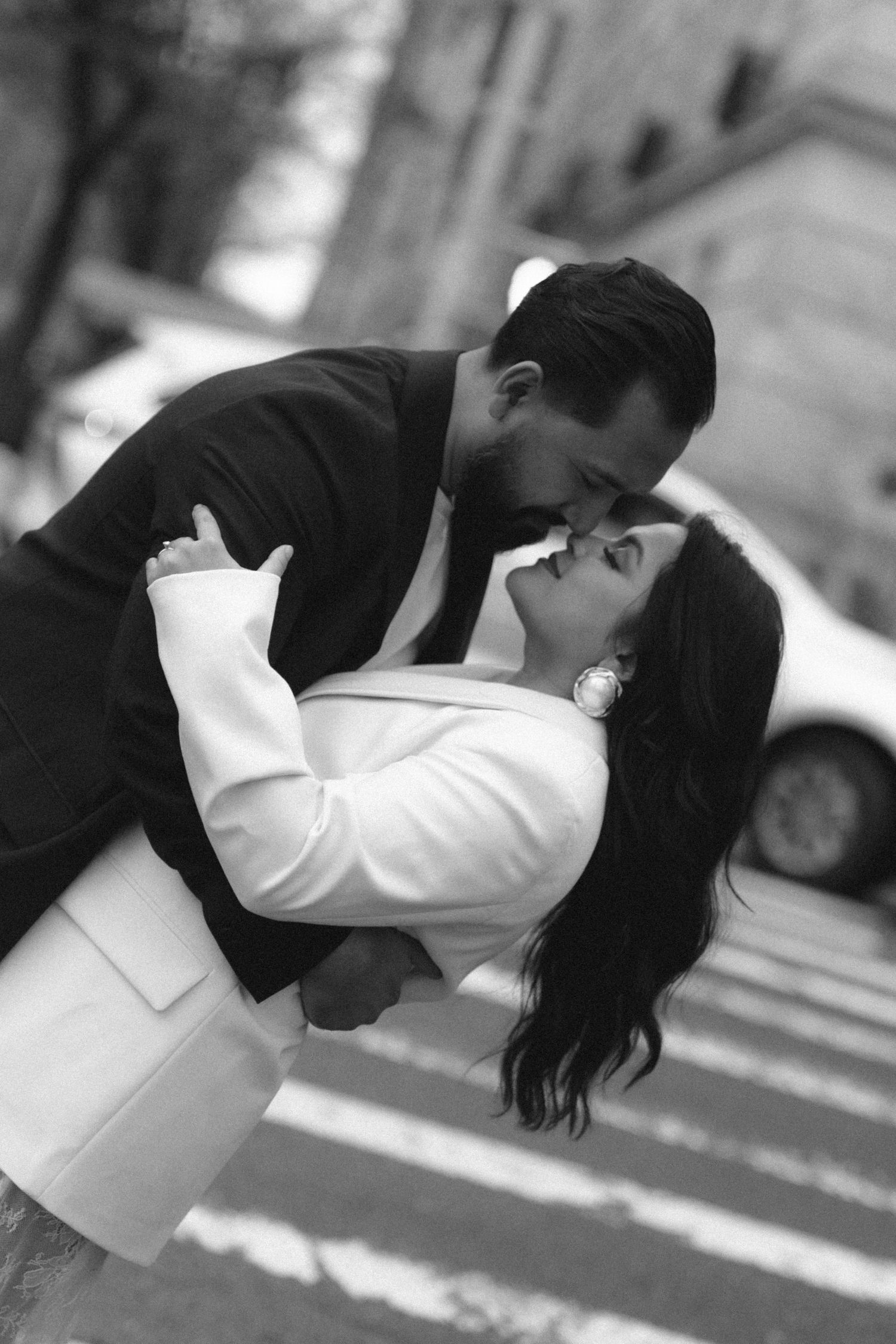 Black and white photo of couple sharing a romantic dip kiss on a city street.
