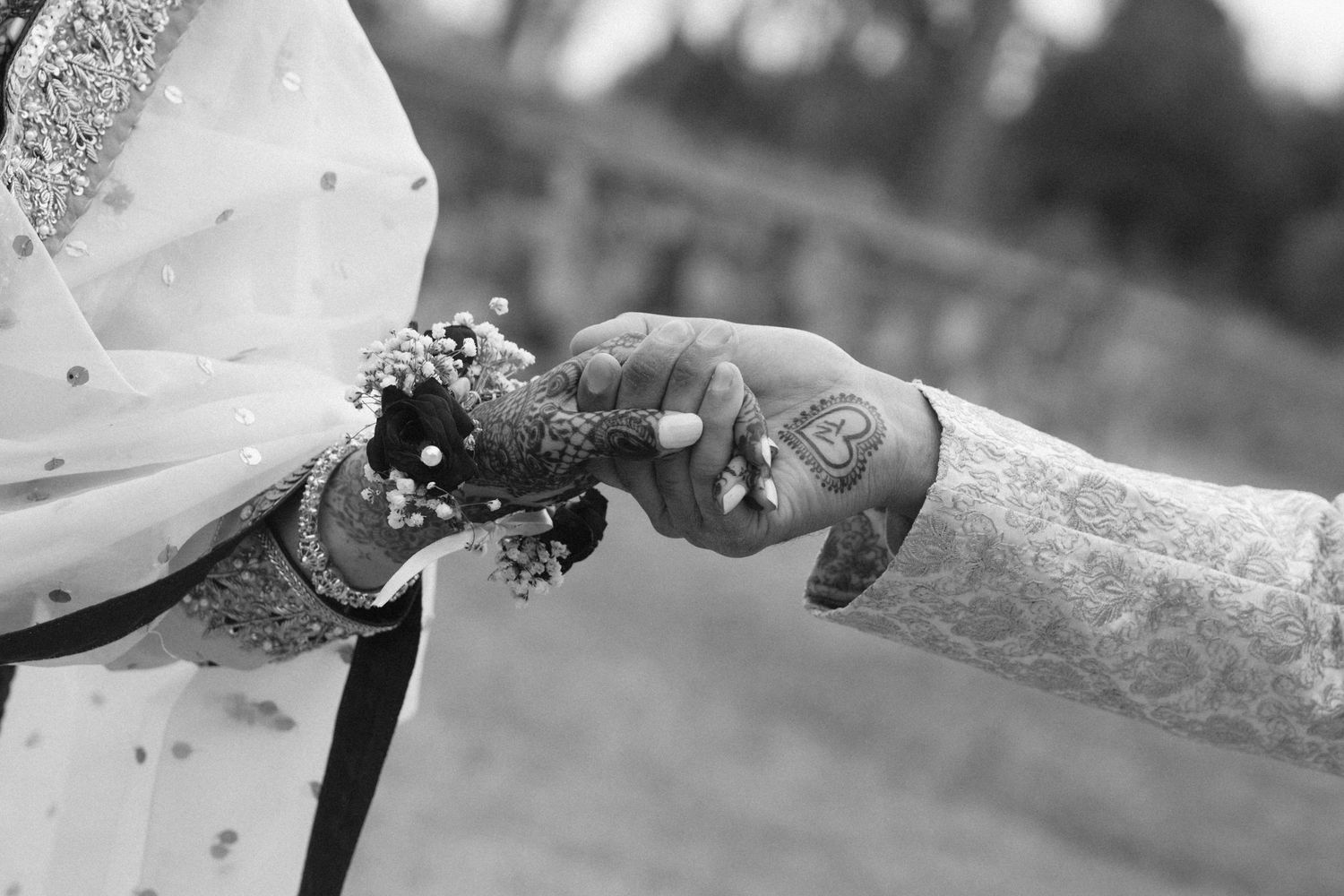 Black and white photo of bride and groom exchanging flowers with henna-adorned hands during Indian wedding ceremony.