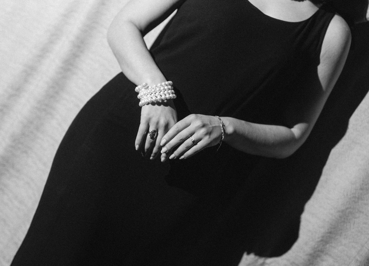 Black and white photo of a woman in a sleeveless black dress wearing pearl bracelets with manicured nails.