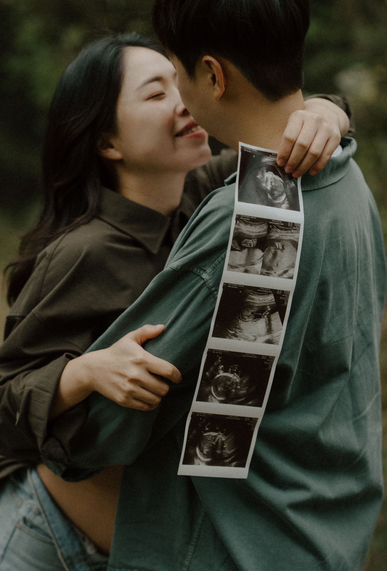 Happy couple embracing outdoors holding ultrasound photos, announcing pregnancy with joy and love.