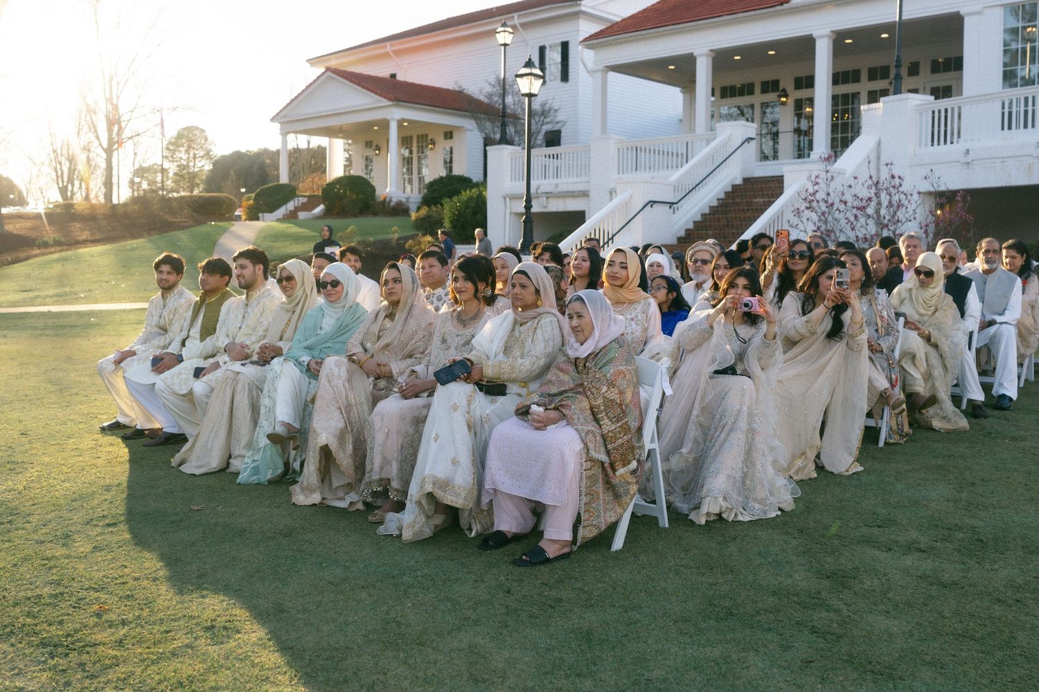 Large group of guests in traditional South Asian attire seated outdoors at an elegant wedding ceremony.