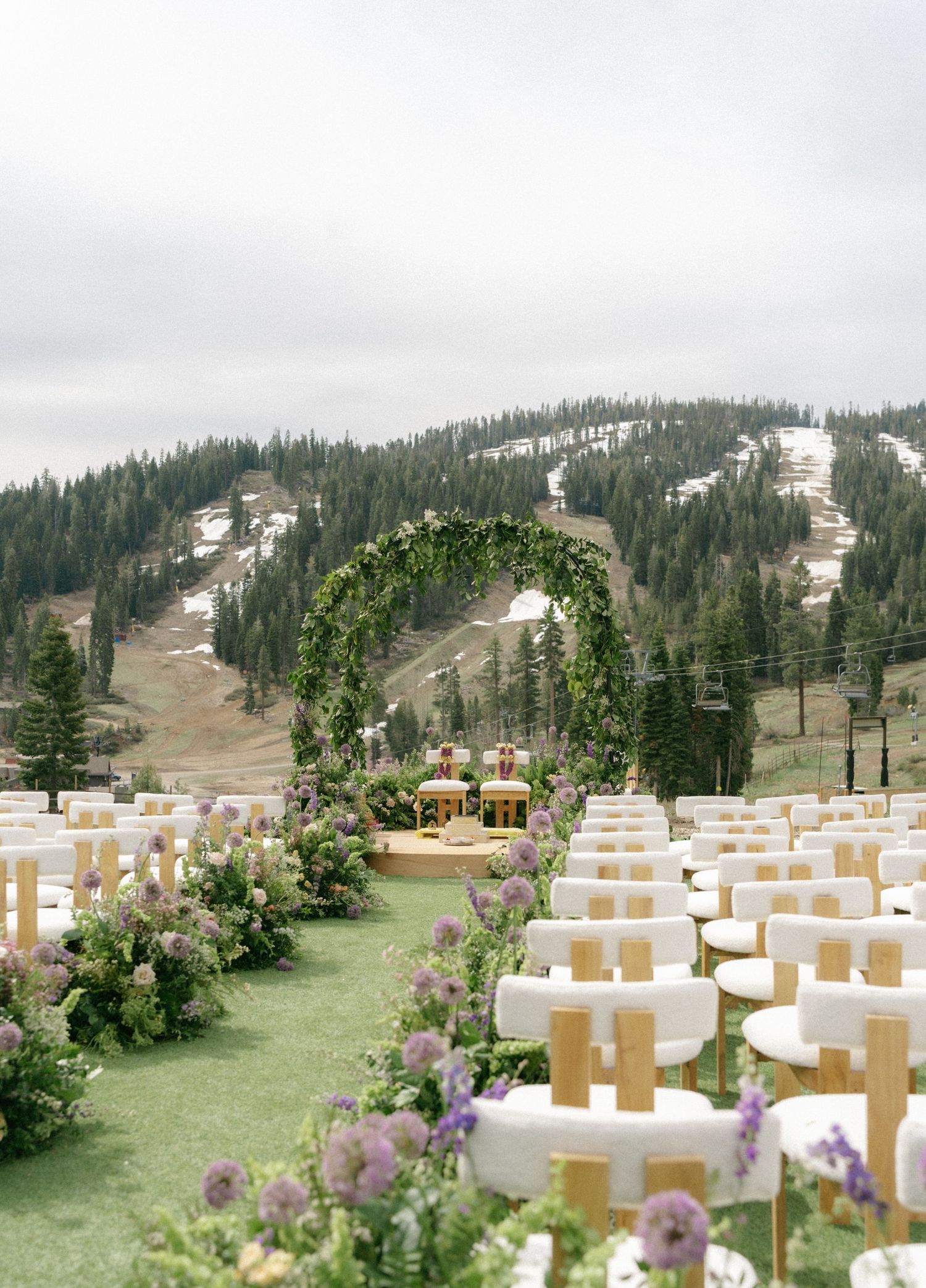 Outdoor wedding ceremony with white chairs, floral arch, and snowy mountain backdrop.