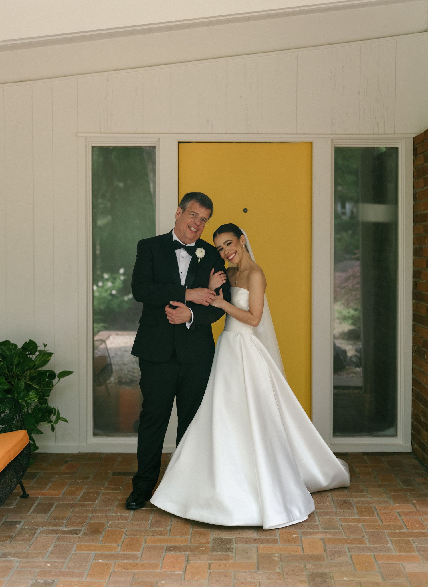 Smiling bride and groom posing together in front of a bold yellow door on their wedding day.