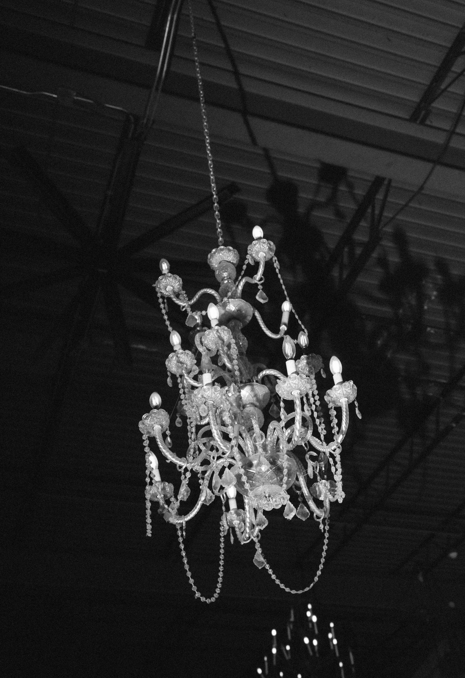 Elegant crystal chandelier with candle-style bulbs hanging from ceiling, captured in black and white photography.