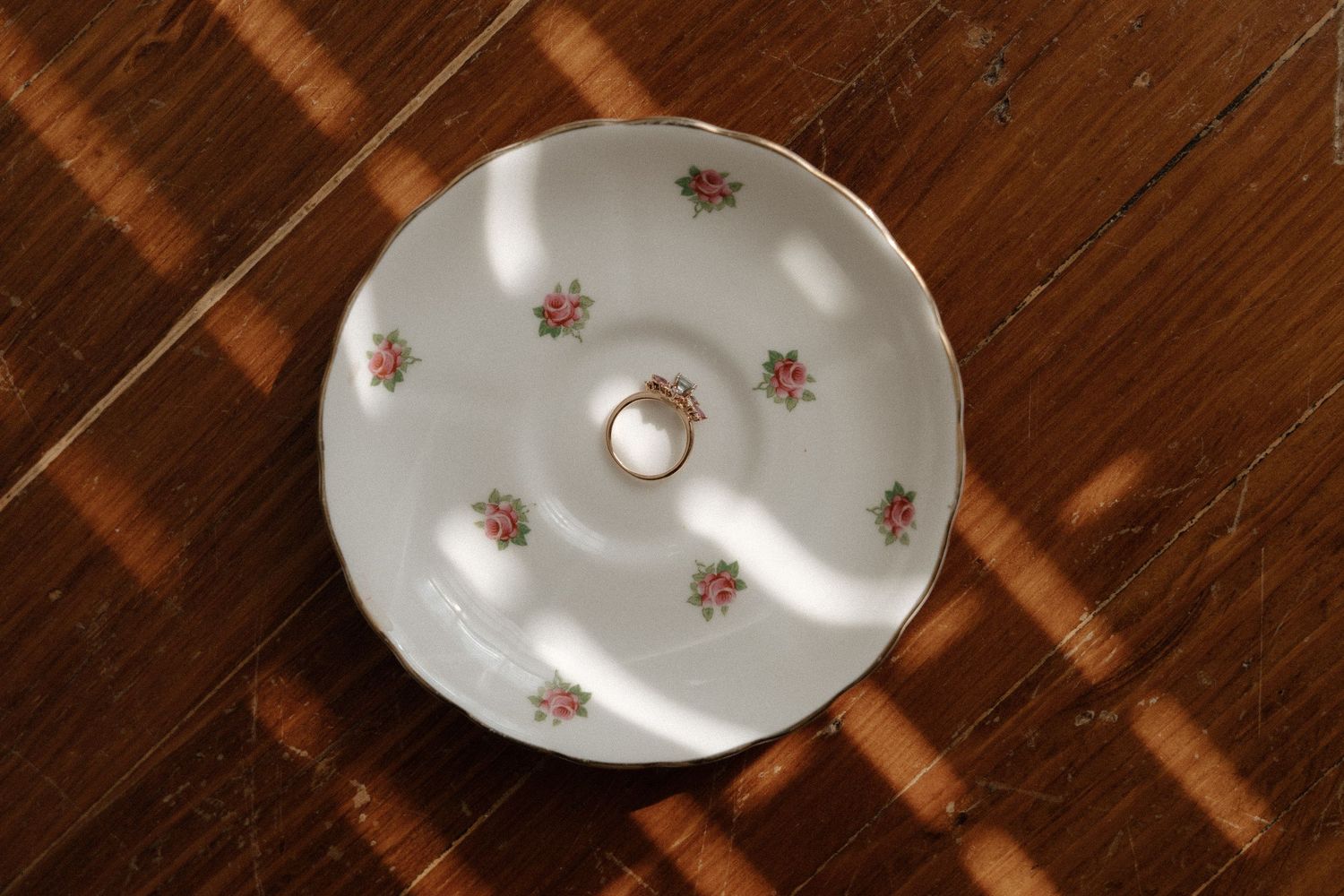 White floral porcelain ring dish with gold trim holding a ring, placed on a wooden surface.