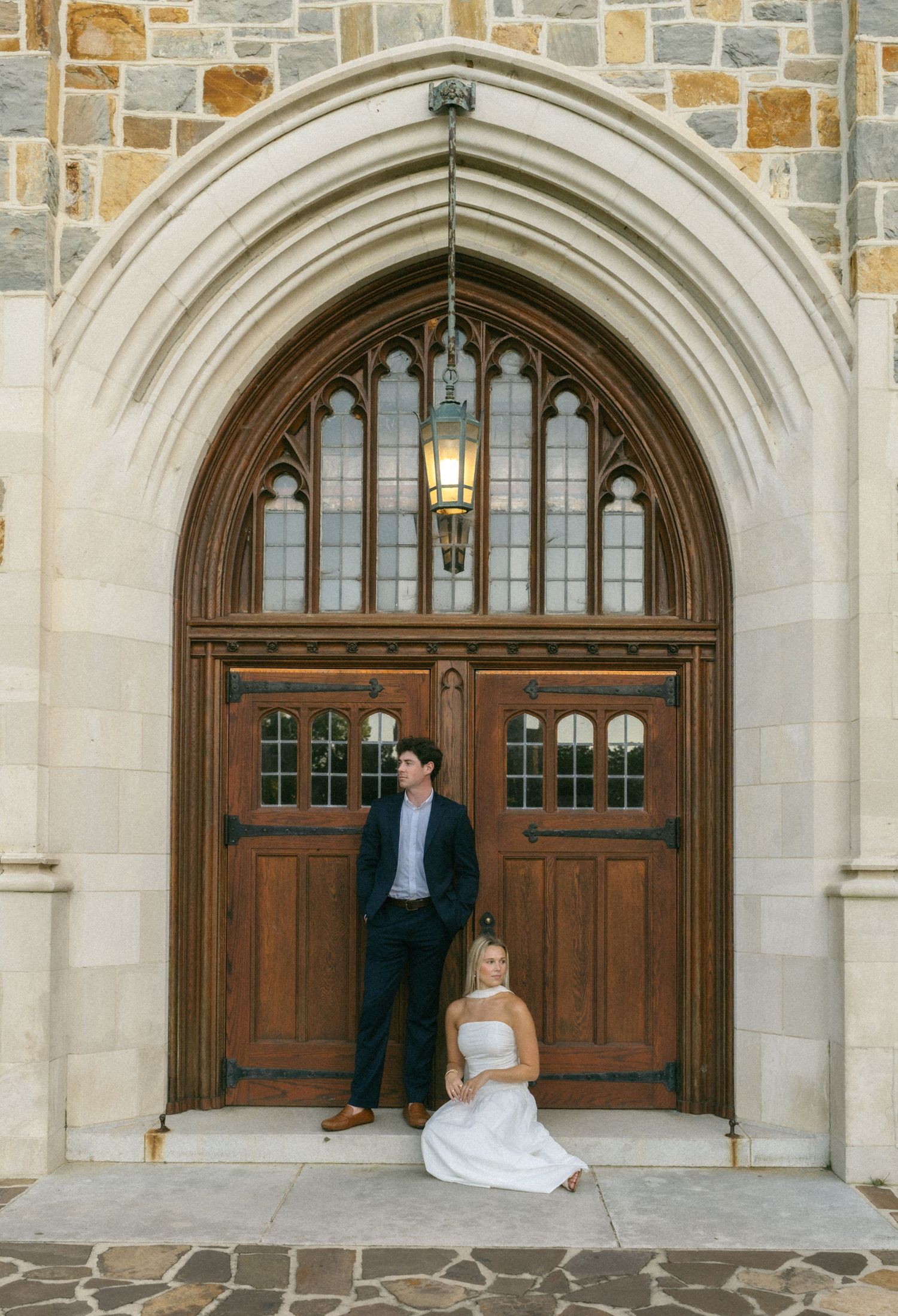 Couple poses before ornate Gothic church wooden doors with stone arch for elegant wedding portrait.