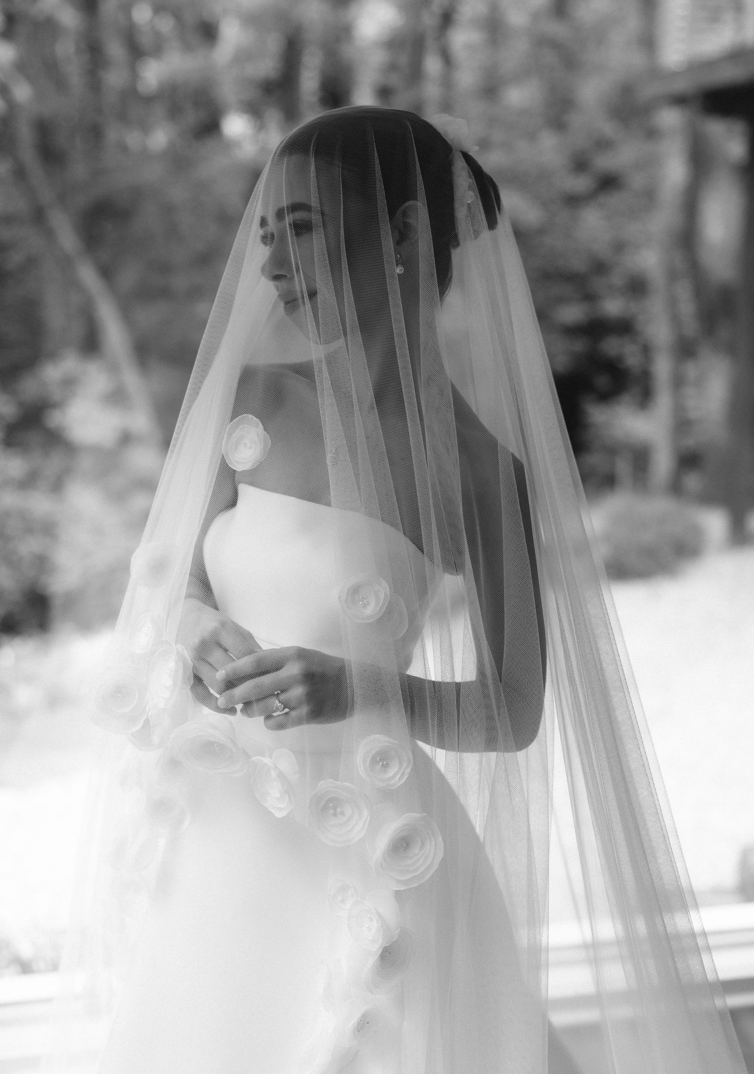Elegant bride in strapless gown with floral details wearing a long flowing veil in a black and white portrait.