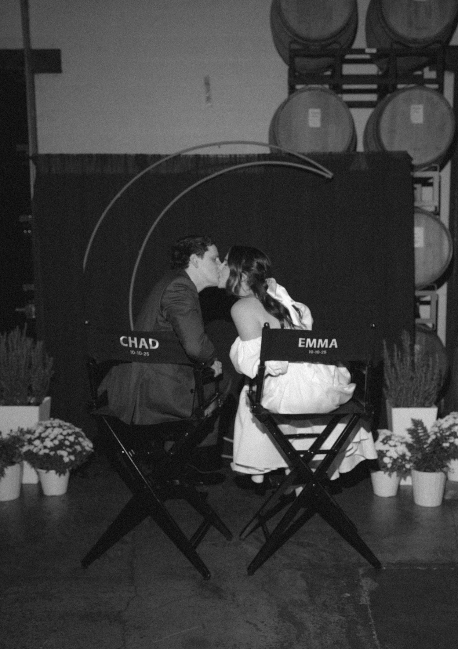 Black and white photo of couple Chad and Emma kissing in director chairs at a winery wedding reception.