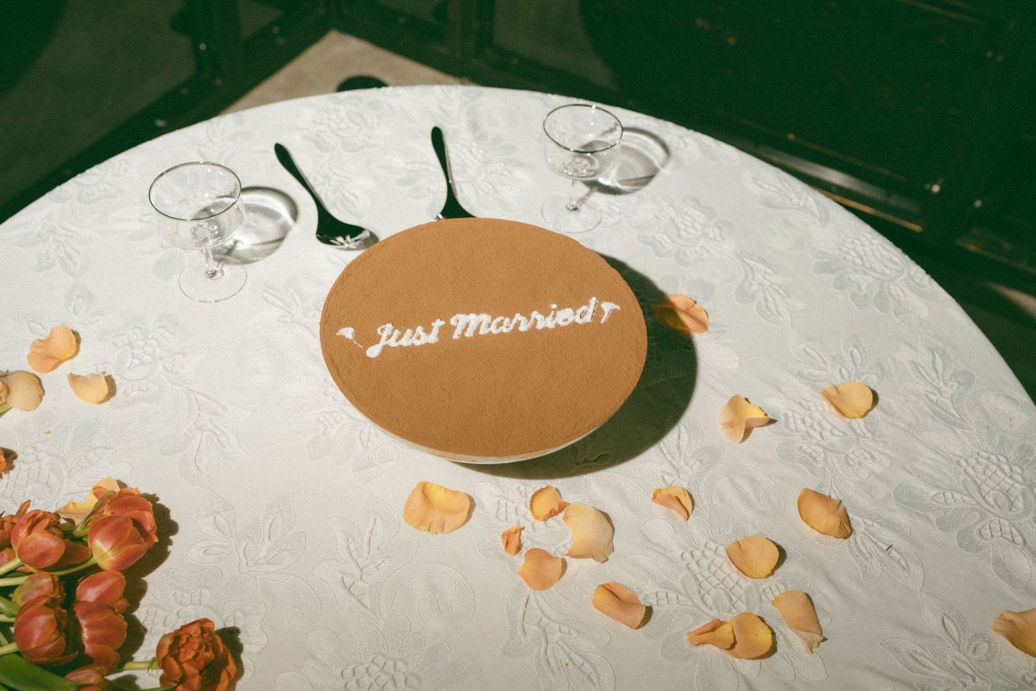 A white round table with a Just Married sign, rose petals, and empty glasses at a wedding reception.