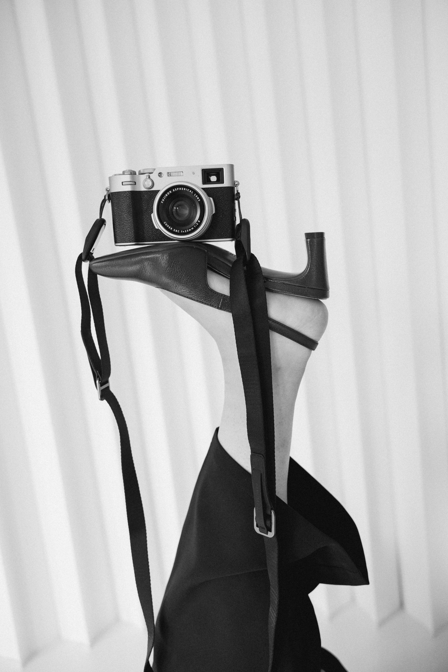 Black and white photo of a vintage camera with strap resting on a clothes hanger with a dark jacket.