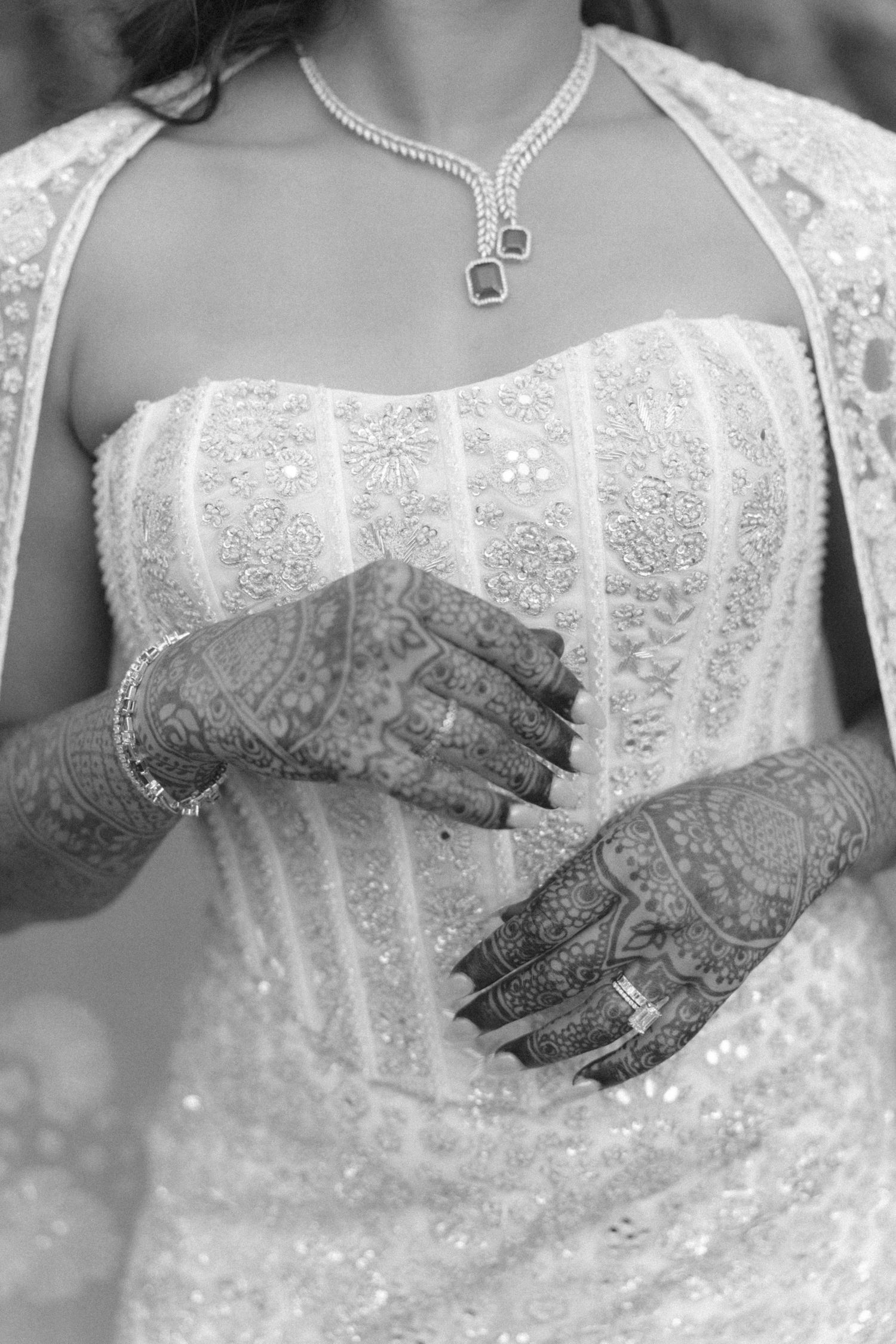 Black and white close-up of Indian bride's hands adorned with intricate mehndi henna designs and diamond jewelry.