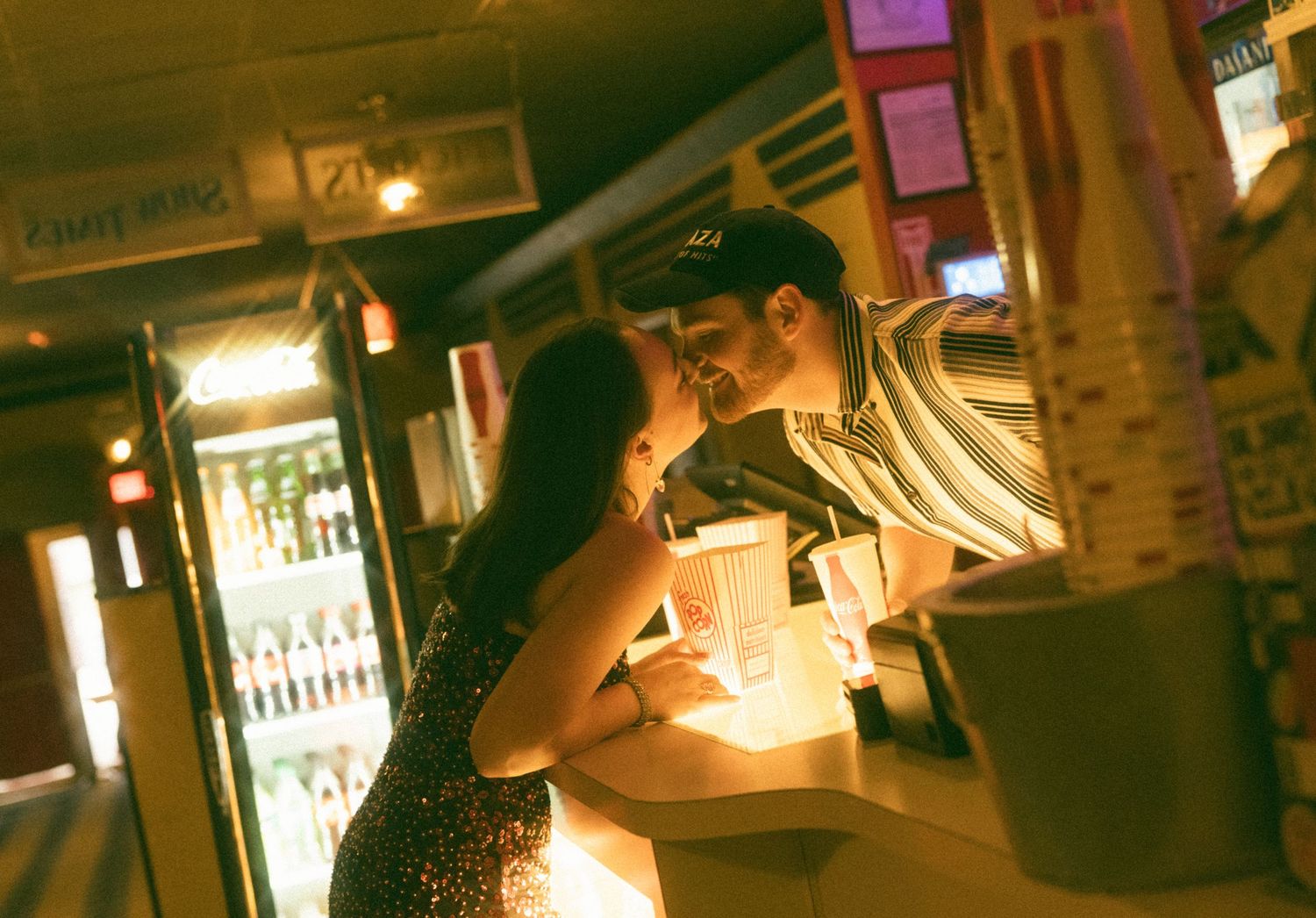 Couple sharing an intimate moment at a dimly lit bar counter with warm amber lighting and refrigerator display.