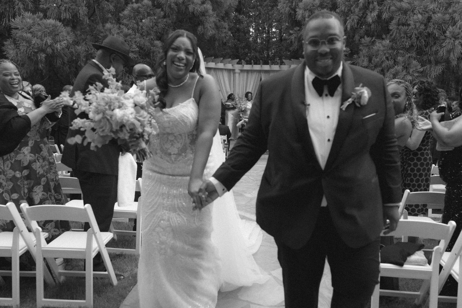 Black and white photo of a joyful bride and groom walking down the aisle after their outdoor wedding ceremony.