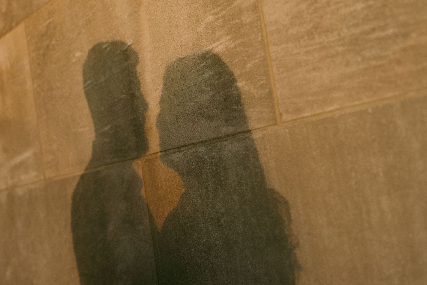 Two people's shadows cast on a warm golden-brown brick wall, creating a romantic silhouette effect.