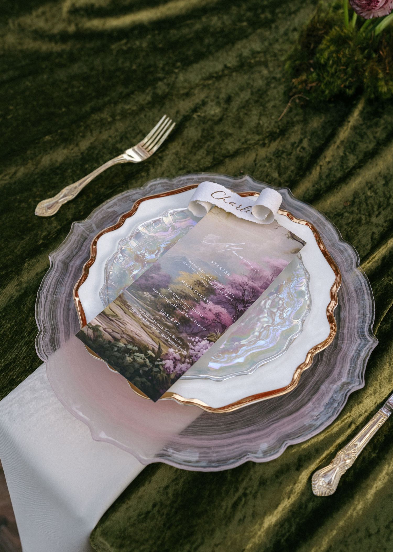 Elegant wedding place setting with agate charger plate, gold-rimmed china, and floral menu card on green velvet.