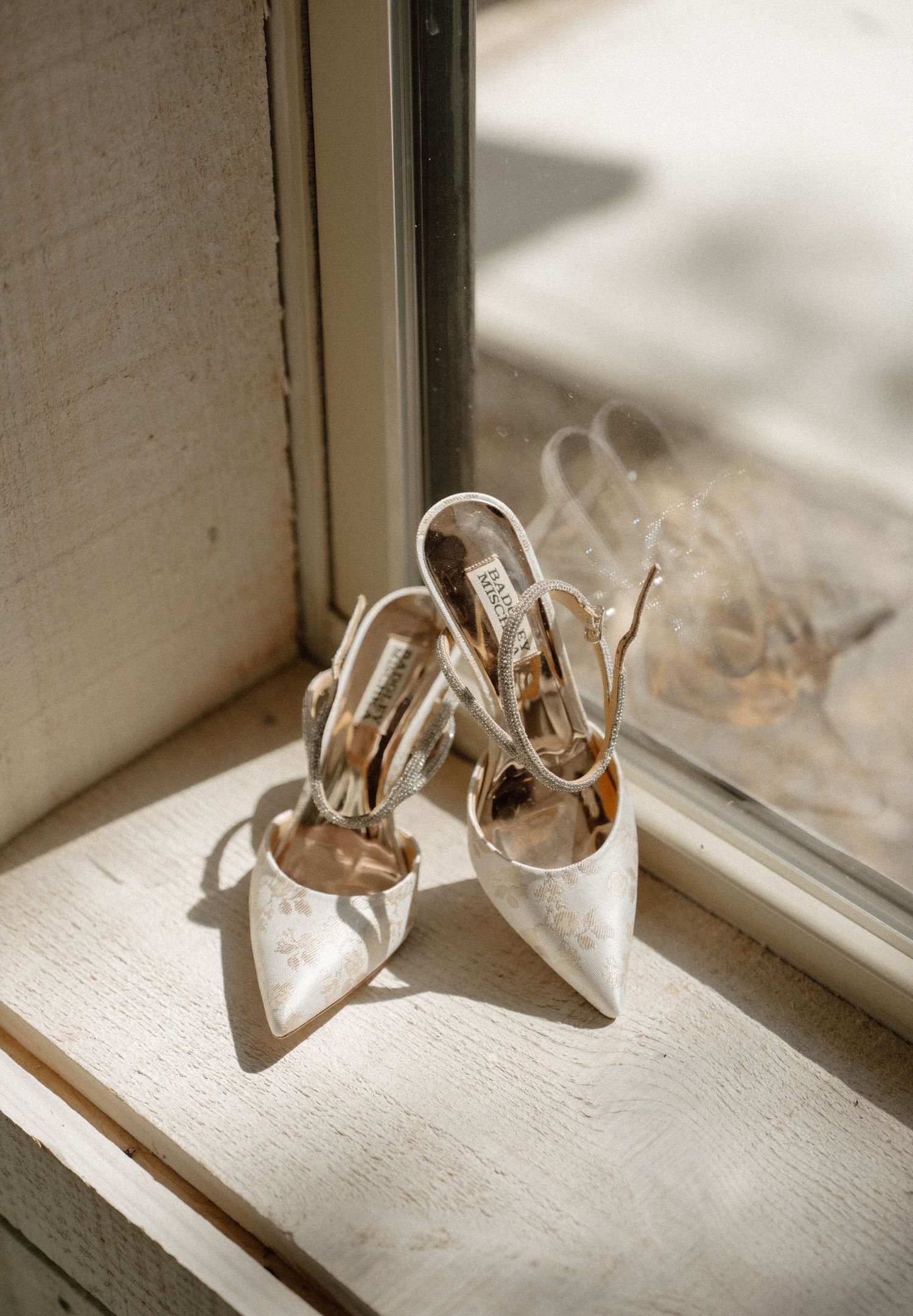 Badgley Mischka bridal slingback heels displayed on a sunlit windowsill.
