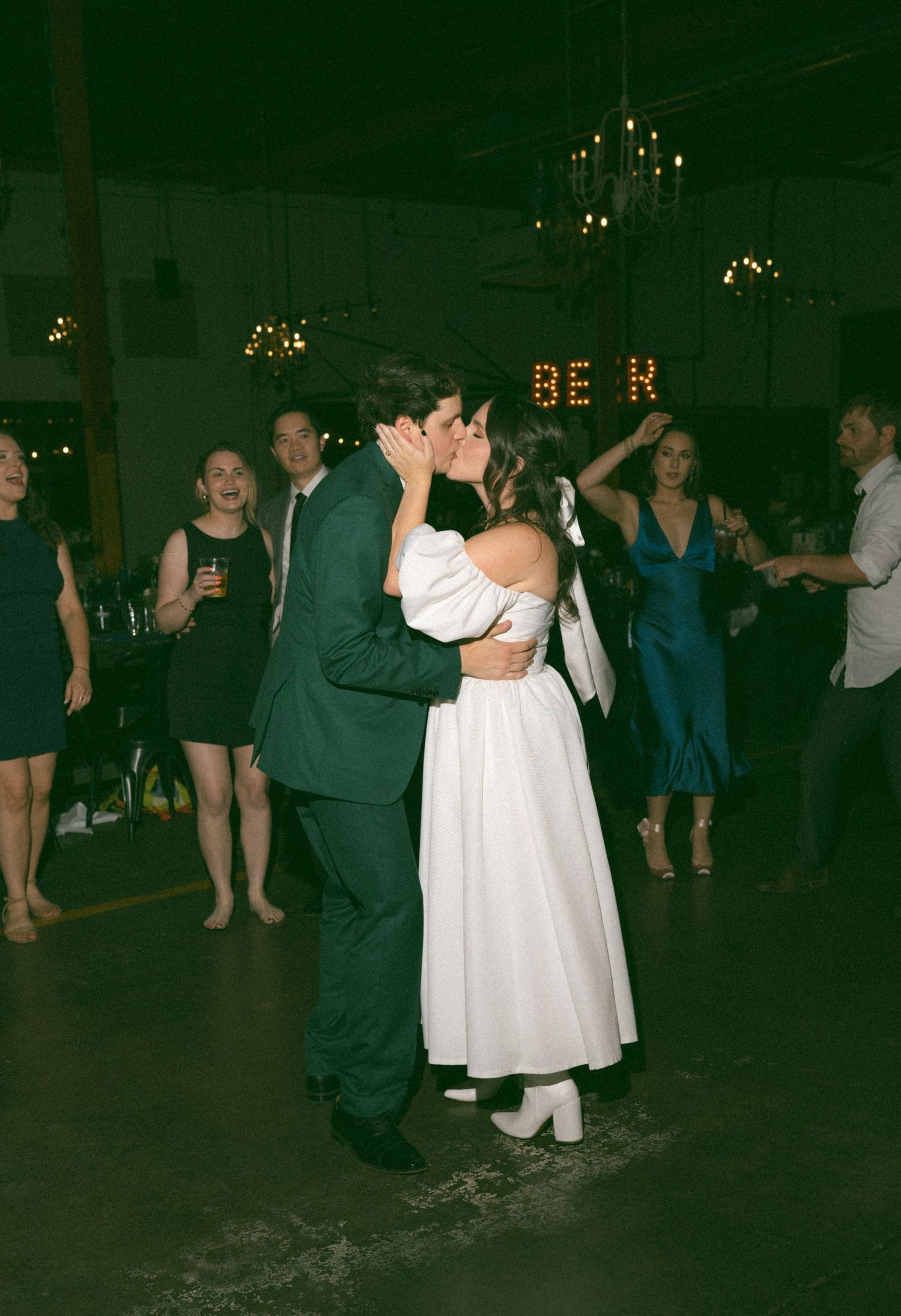 Bride and groom share a kiss on the dance floor at their wedding reception surrounded by guests.