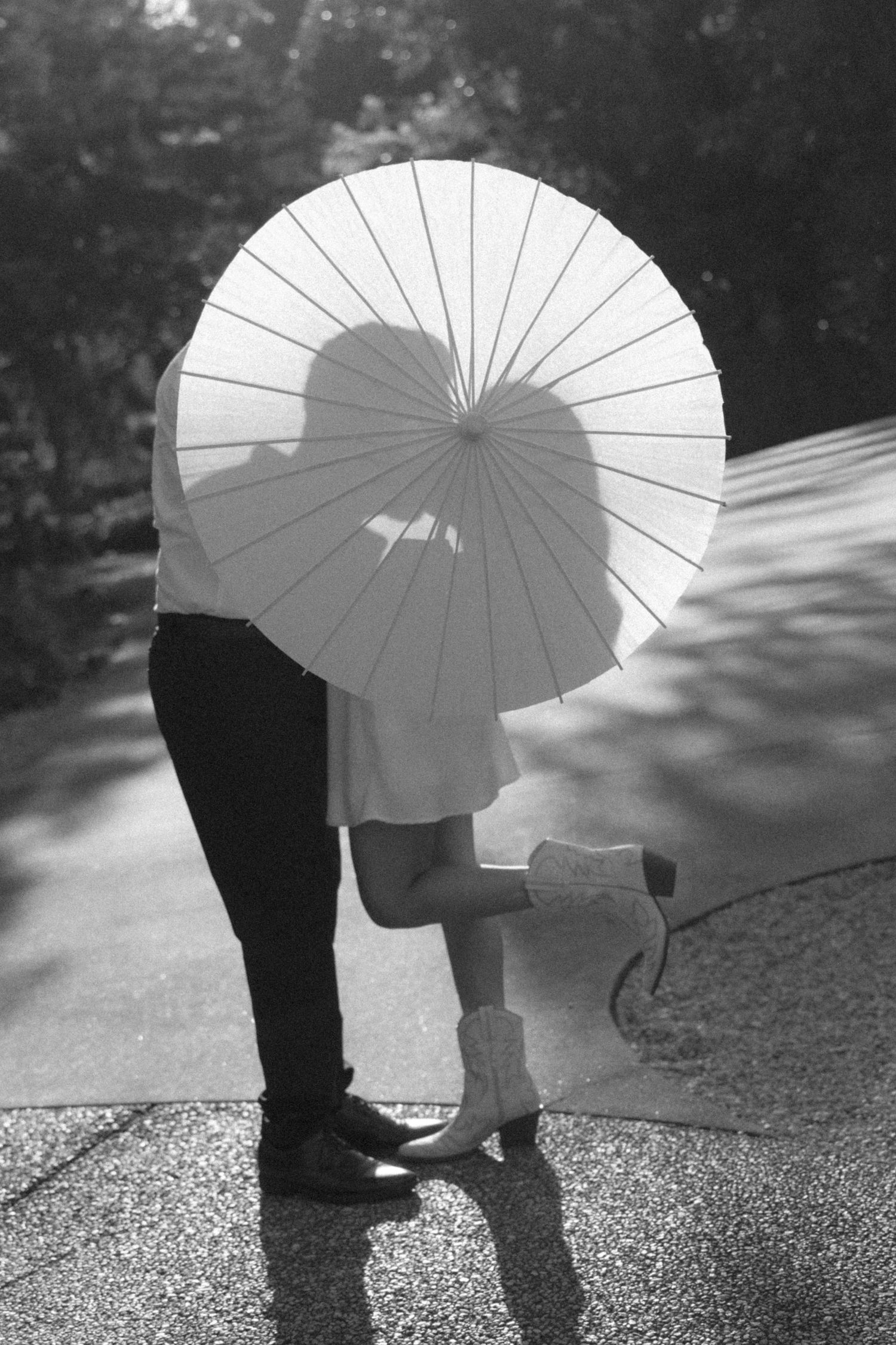 Couple kissing behind a white paper parasol umbrella outdoors, black and white romantic photo.