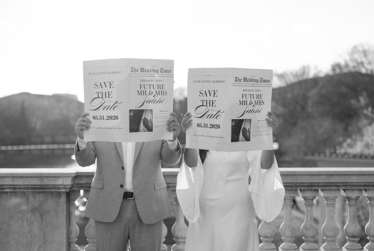 Couple holds Save the Date newspapers in black and white wedding photo outdoors.