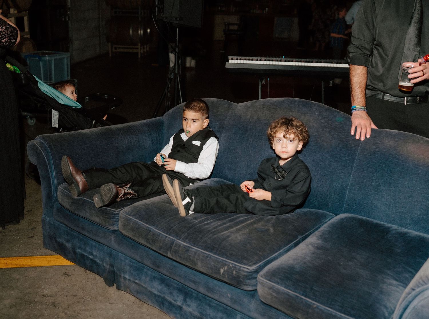 Two young boys in formal attire sitting on a blue velvet sofa at an indoor event.